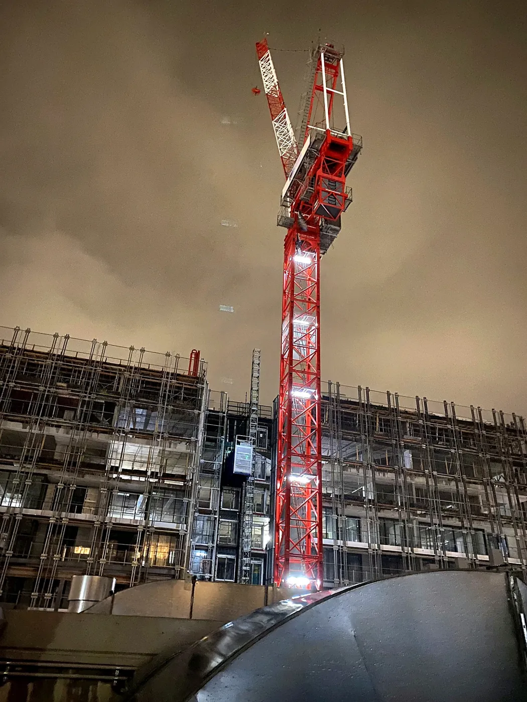 Red tower crane lit at night above a multi-storey commercial building under construction